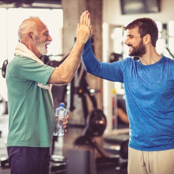 Personal trainer talking and with senior man at gym.
