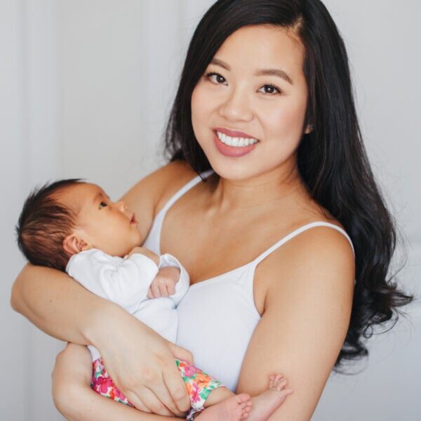 Portrait of beautiful smiling Chinese Asian mother holding cute adorable newborn infant baby son daughter. Happy family in bedroom. Home lifestyle authentic natural moment. Mothers day.